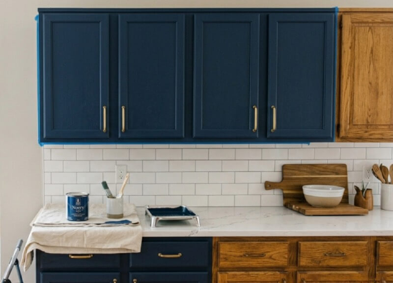 Close-up of a freshly painted modern navy kitchen cabinet next to an original unfinished oak cabinet, showing the smooth urethane finish.