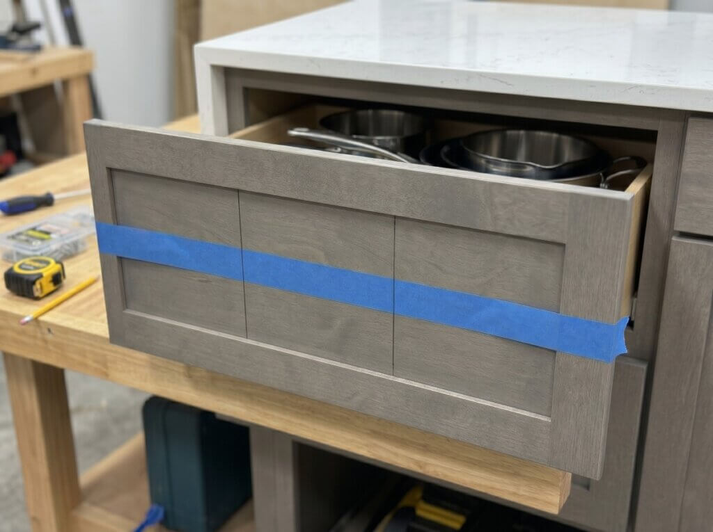 A wide kitchen drawer with blue painter's tape and pencil marks dividing it into three equal sections.